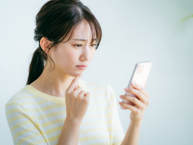 スマホの画面を見て悩む女性