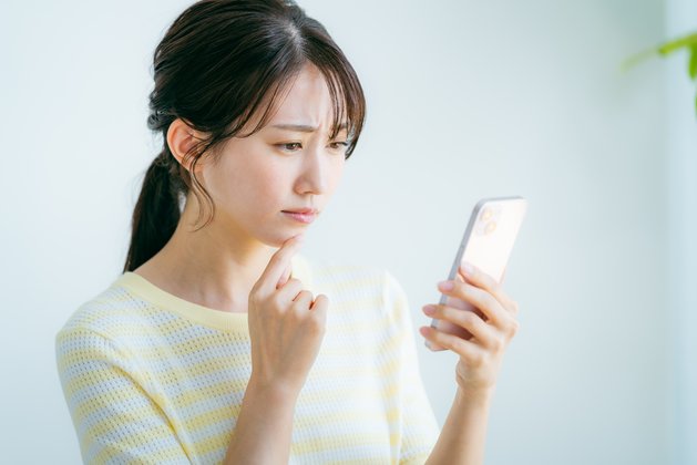 スマホの画面を見て悩む女性